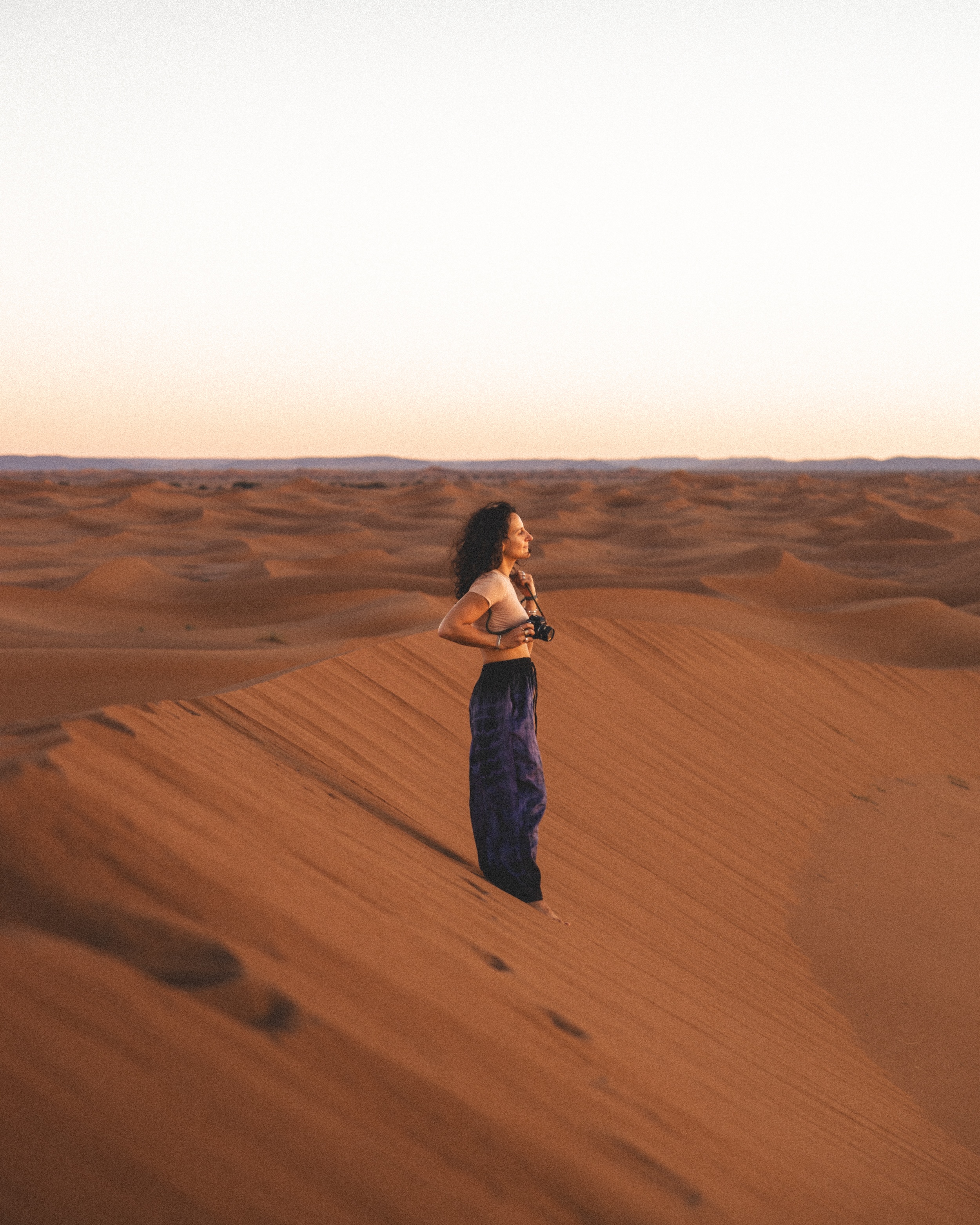 Ilaria Ronchi standing amidst desert dunes, holding her camera, embodying the fusion of photography and architectural design