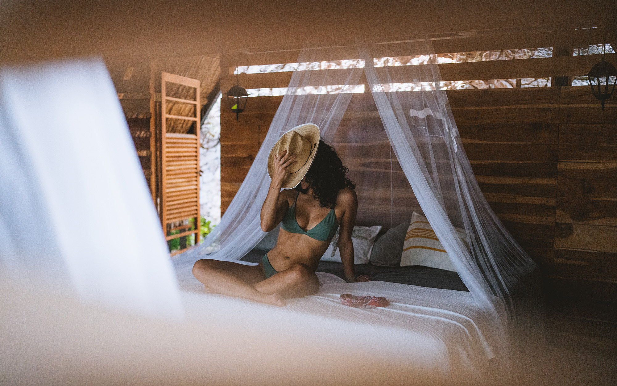 Woman in a bikini sitting under a mosquito net in a bedroom at Azul Nomeolvides Hotel, Bacalar, Mexico