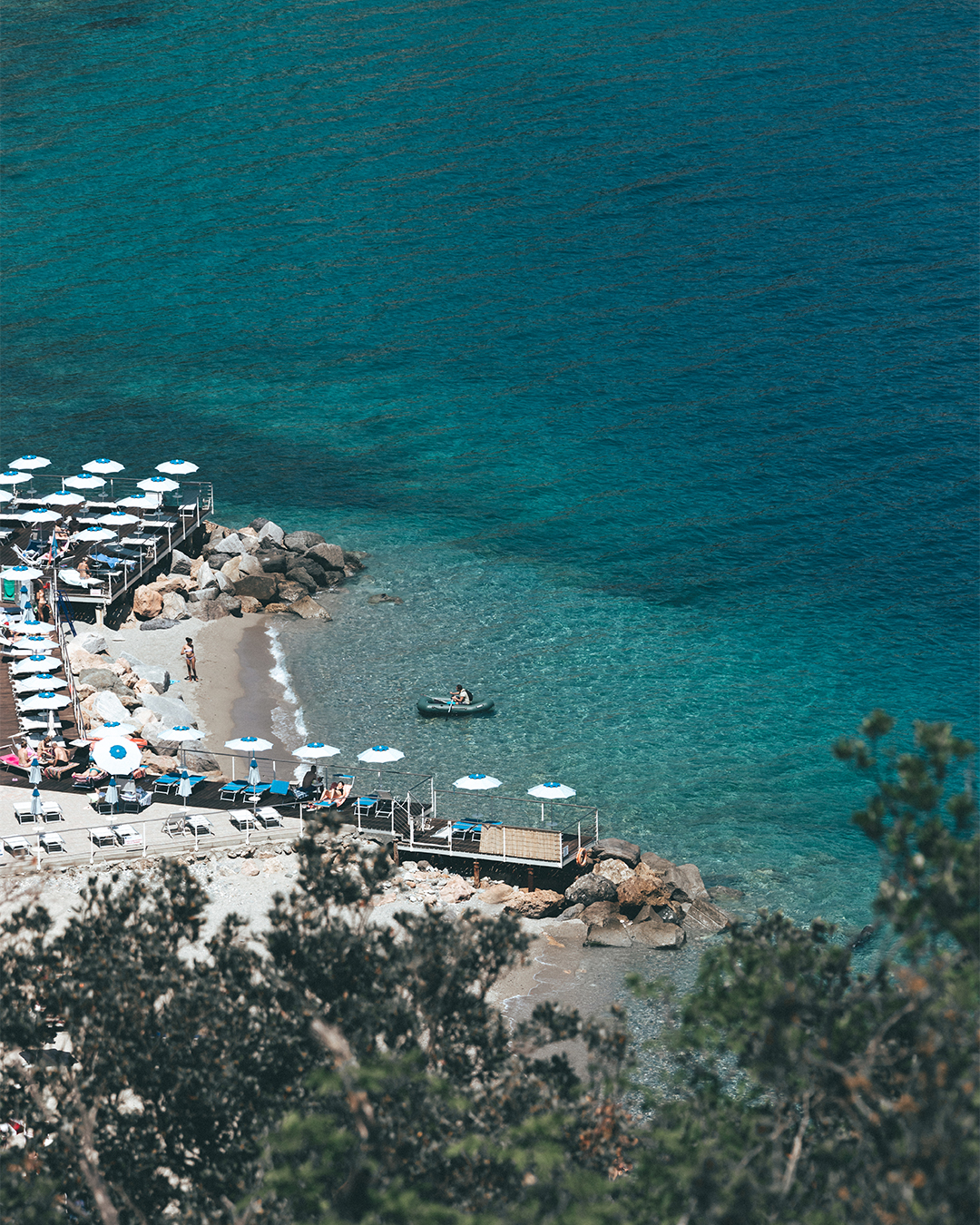 Aerial view of Noli Beach on the Liguria coast, Italy, with clear turquoise waters and sunbathers