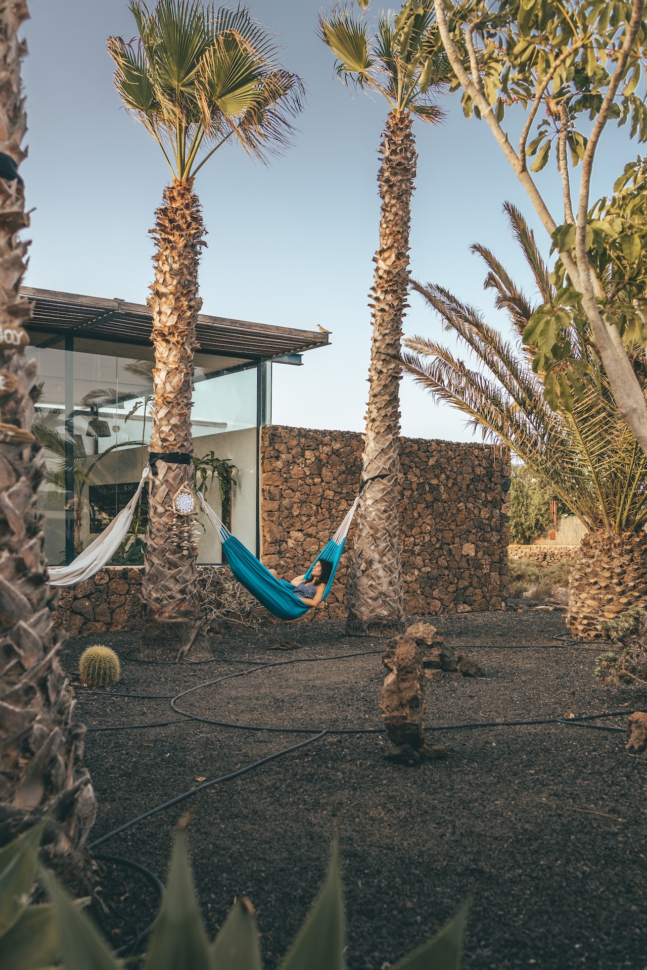 Person relaxing in a hammock at a yoga surf villa in Fuerteventura, surrounded by palm trees