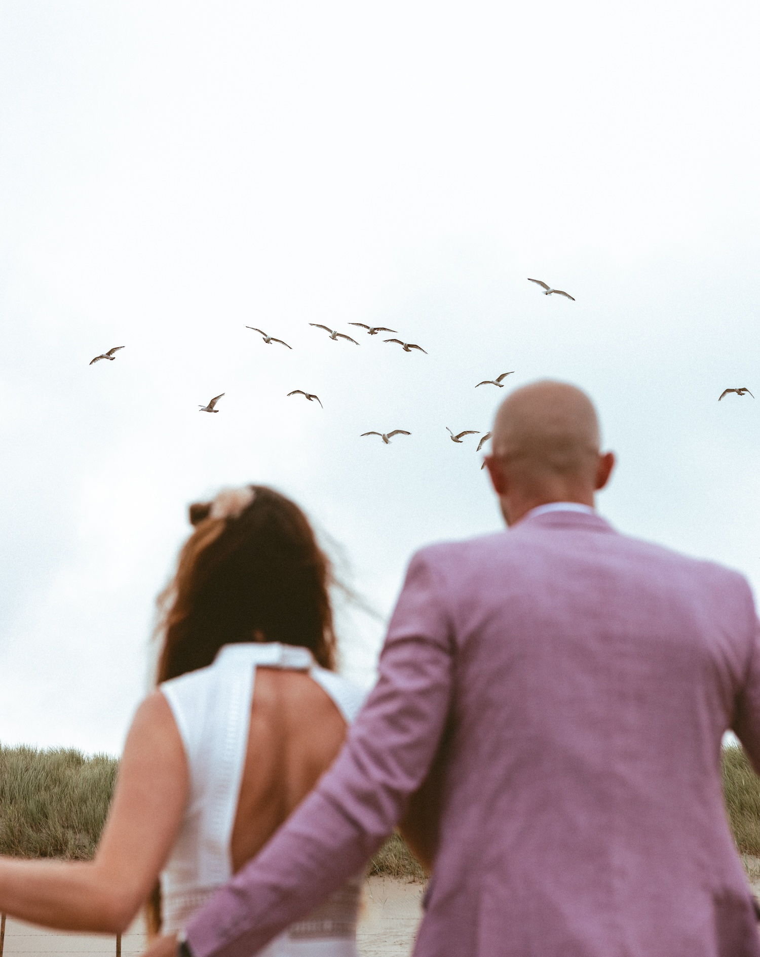 A couple walking hand in hand, surrounded by a serene beachscape with birds flying in the background