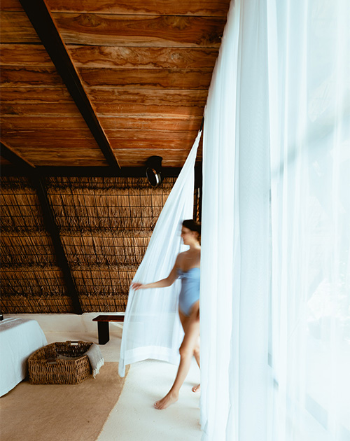 Whimsical motion of a woman behind sheer gauze curtains in a rustic A-frame cabin interior