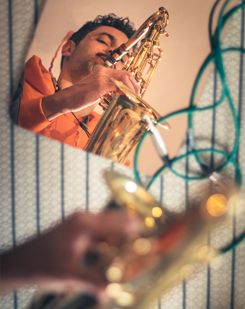 Intimate view of Dillon playing the saxophone behind a textured screen