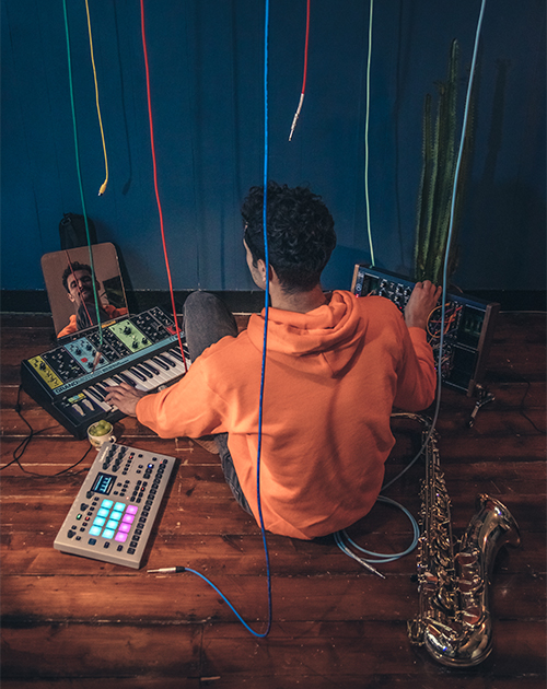 Musician Dillon engrossed in a music production session with synthesizers and a saxophone