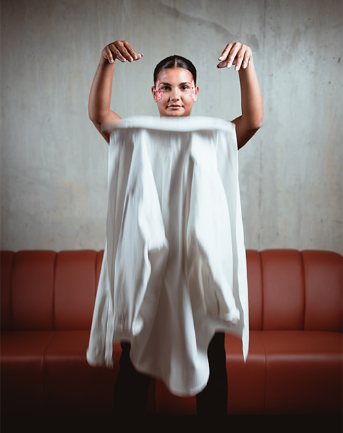 Creative portrait of a model holding a floating white fabric with a textured concrete backdrop