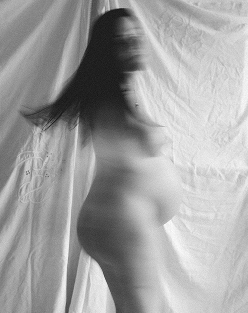 Ethereal motion blur of a pregnant woman's figure against a crinkled backdrop