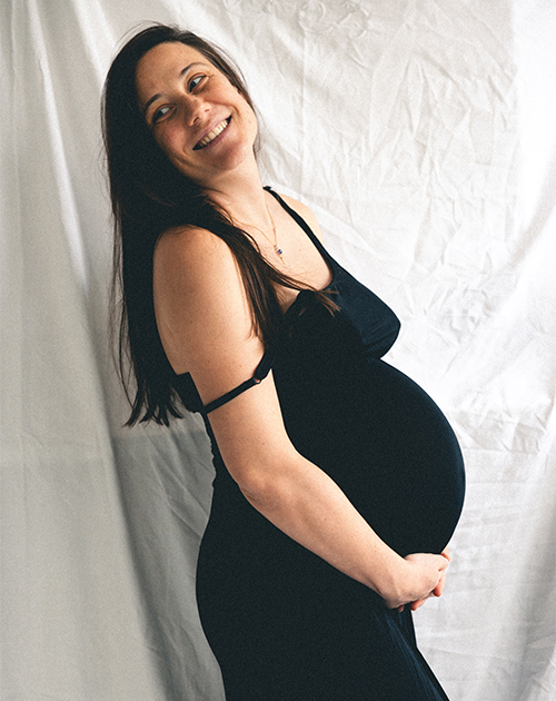 Joyful expectant mother in a black dress with a heartwarming smile, cradling her bump