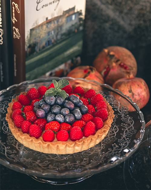 Artistic display of a berry tart with ripe pomegranates and cookbook in the background