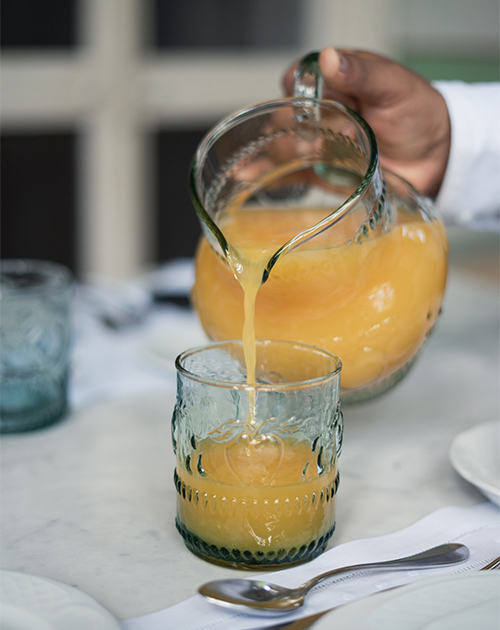 Refreshing orange juice being poured into a glass on a marbled table setting