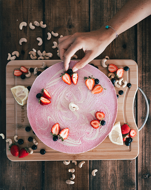 British vegan chef Maddie artfully decorating a vibrant pink plant-based cake with fresh strawberries and blueberries, captured in Fuerteventura