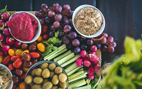 A feast for the eyes, a spread of Maddie's colorful vegan dishes, including vibrant dips and fresh vegetables, showcasing the freshness at a Fuerteventura retreat