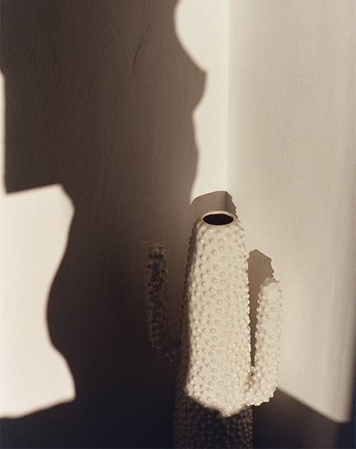 The textured shadow of a woman castt on a white wall in an analog photo, capturing the timeless charm of a Mykonos house