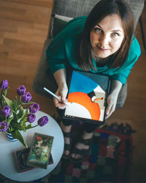 Graphic artist Visnja with a digital tablet creating vibrant digital art, surrounded by the cozy ambiance of her Rotterdam workspace