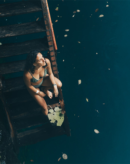 A peaceful moment of contemplation by a serene cenote, as a visitor sits on a wooden ledge in the natural wonders of Yucatan