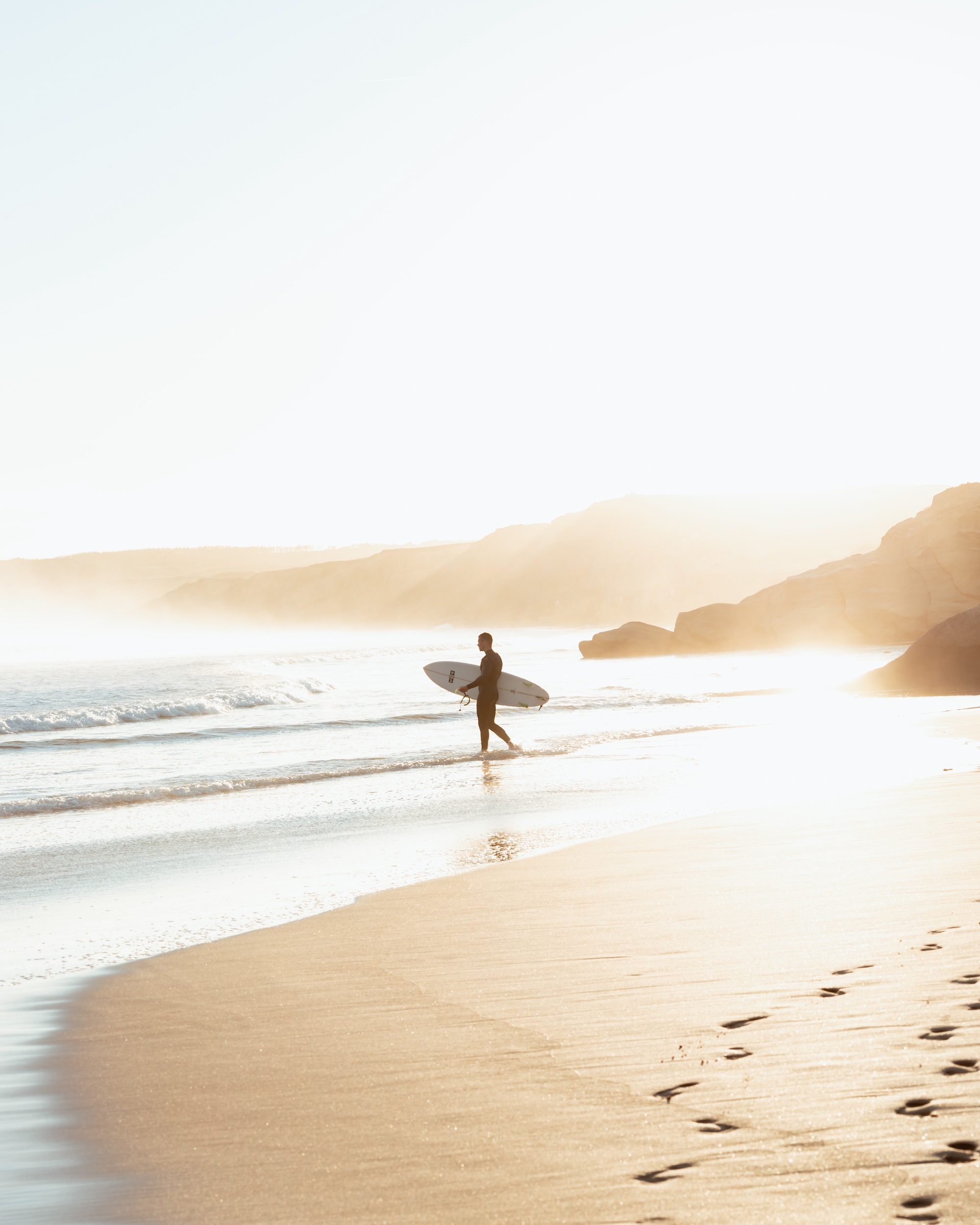 A surfer walks along the shore with his surfboard in Baleal, Peniche